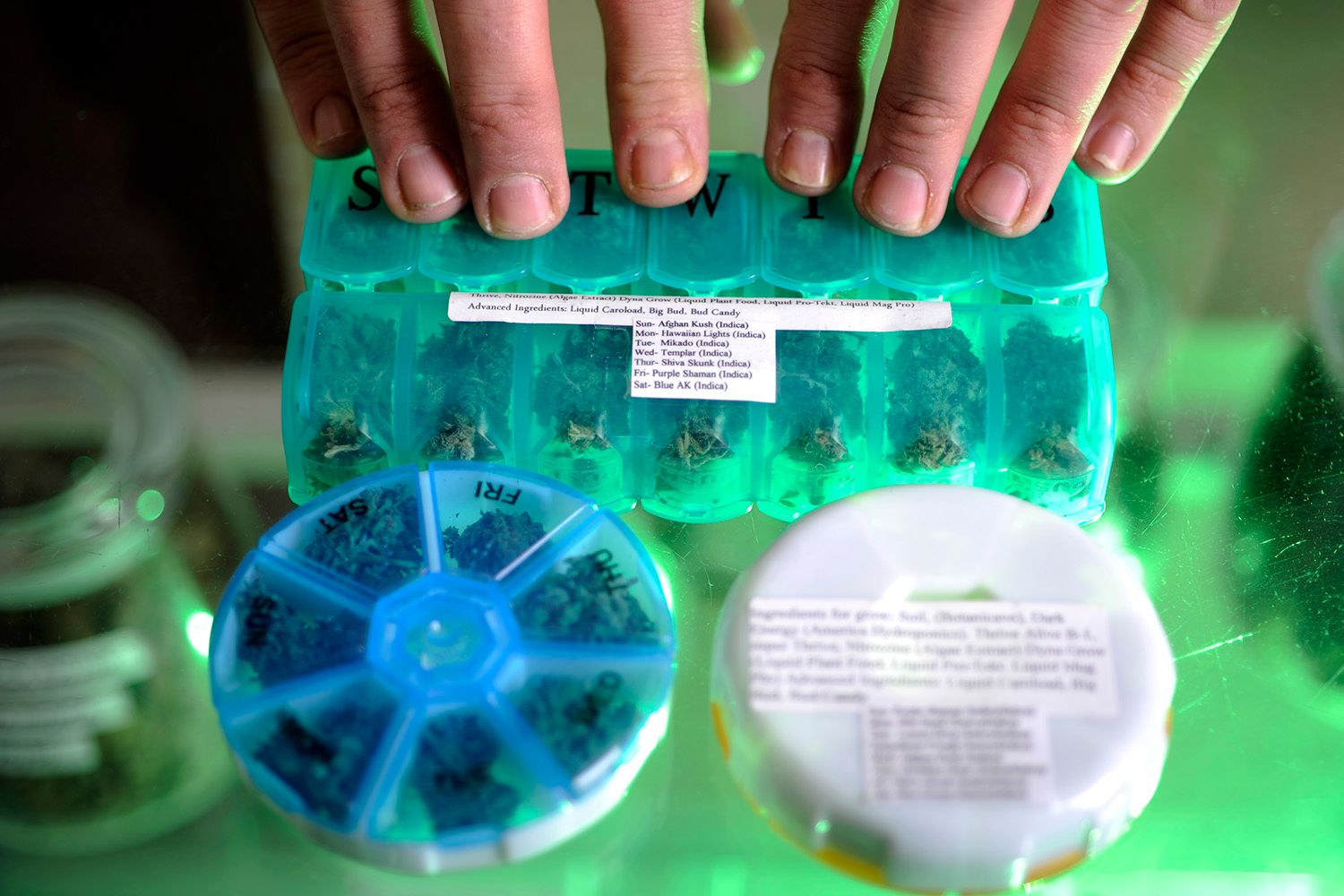 Colored plastic pill containers filled with weed, glass counter top.