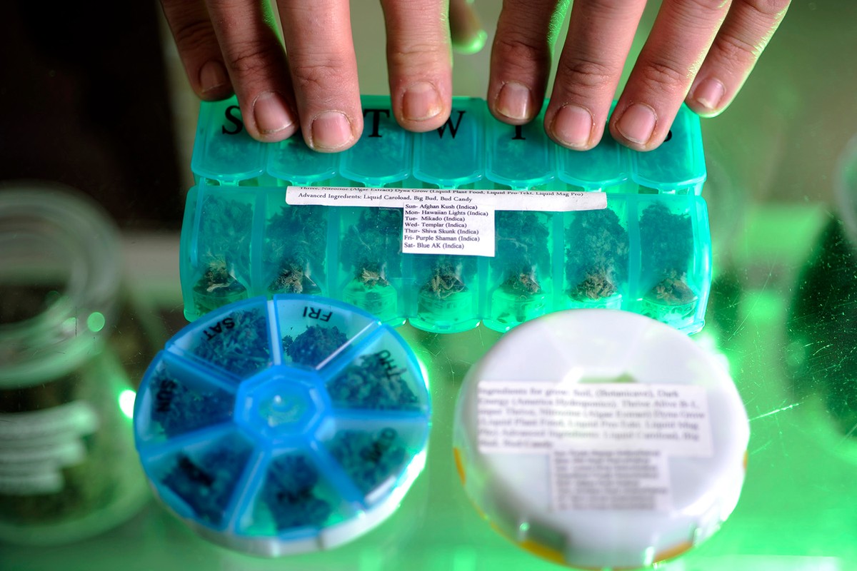Colored plastic pill containers filled with weed, glass counter top.
