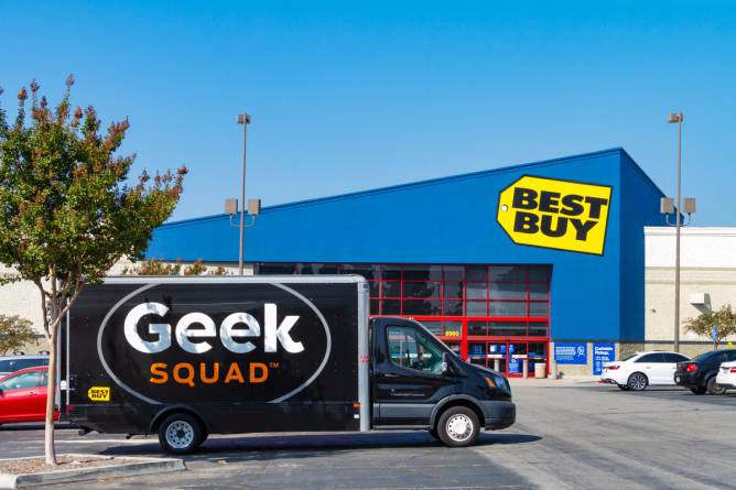 A black Geek Squad van parks outside a Best Buy store.