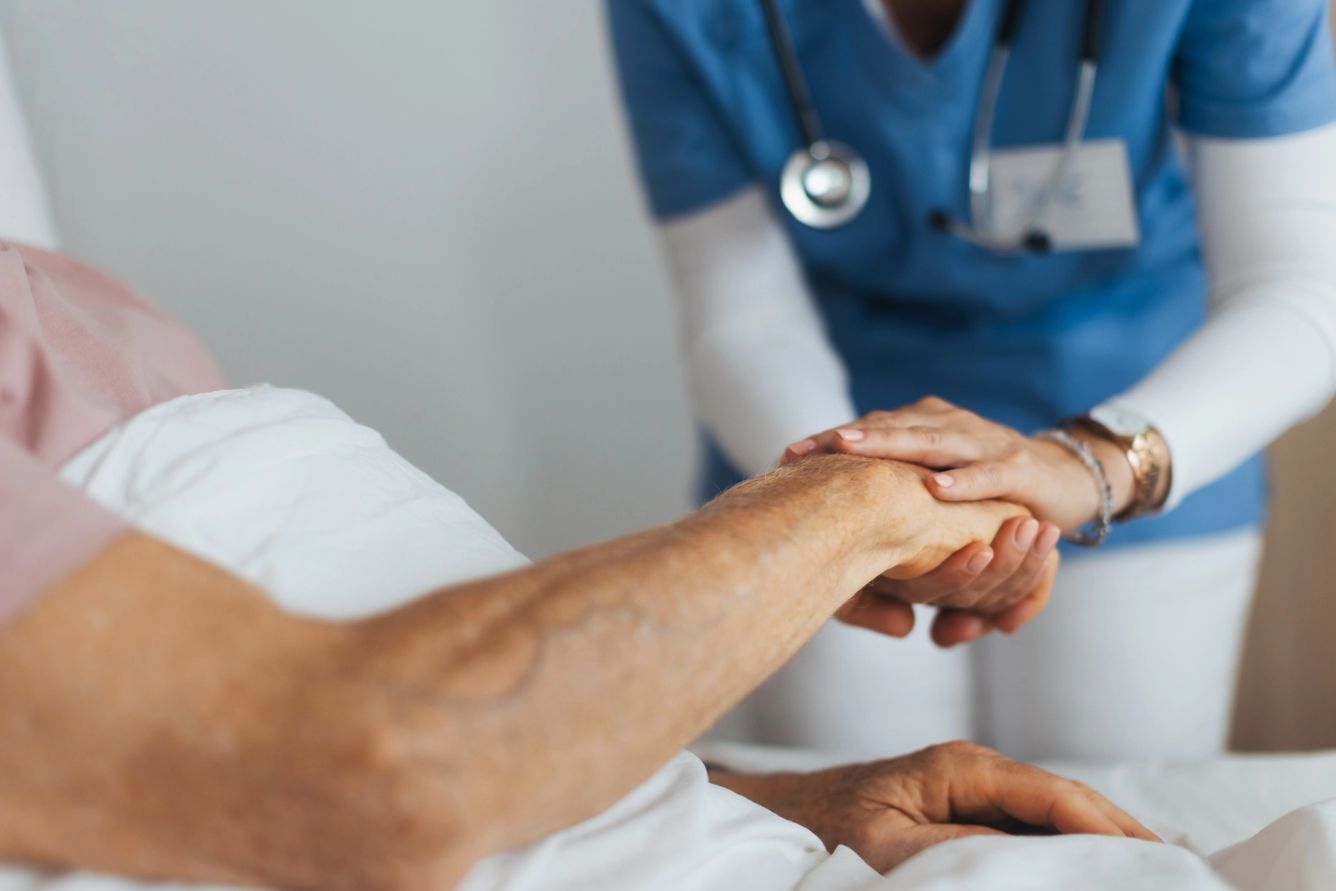 Caregiver holding an elderly patient's hand at their bedside