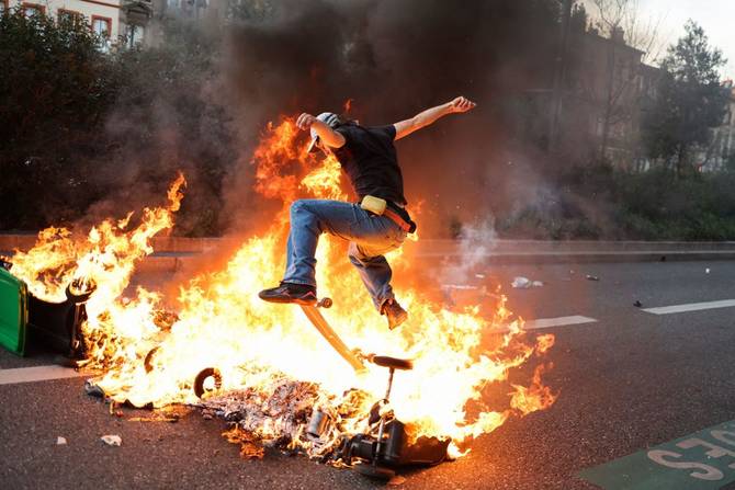 A protestor rides with a skateboard, over burning garbage bins during a demonstration after the government pushed a pensions reform through parliament without a vote, using the article 49.3 of the constitution, in Toulouse