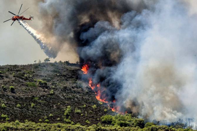 A Sikorsky firefighting helicopter drops water on a wildfire near Agioi Theodori, some 70 kms west of Athens on July 18, 2023