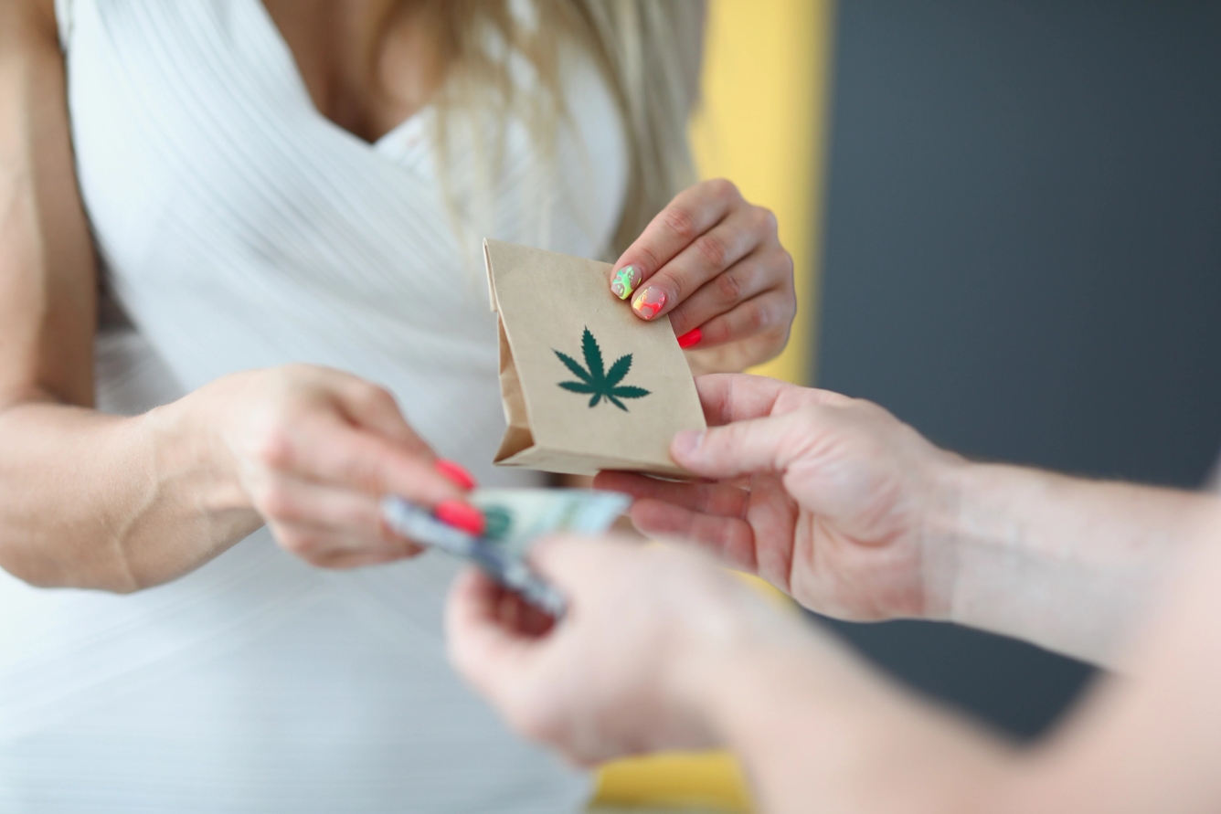 A store clerk hands a customer a shopping bag printed with a cannabis leaf. 