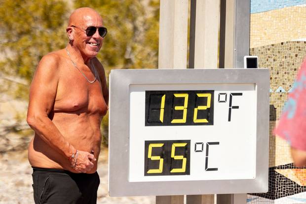 A visitor poses in front of a thermometer reading 132 degrees Fahrenheit and 55 degrees Celsius at the Visitor Center in Death Valley National Park, near Furnace Creek,