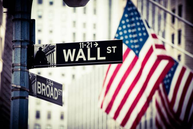 The intersection of Wall Street and Broad Street with an American flag in the background.
