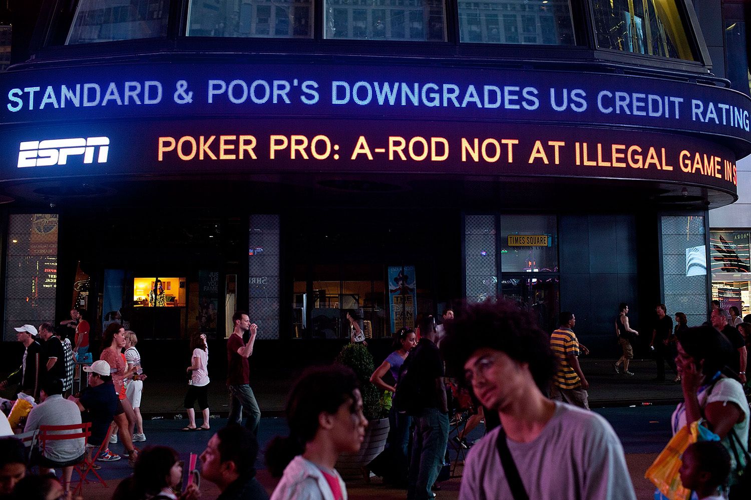 Neon marquee reads 'Standard & Poor's Downgrades US credit rating', busy city street, pedestrians in motion