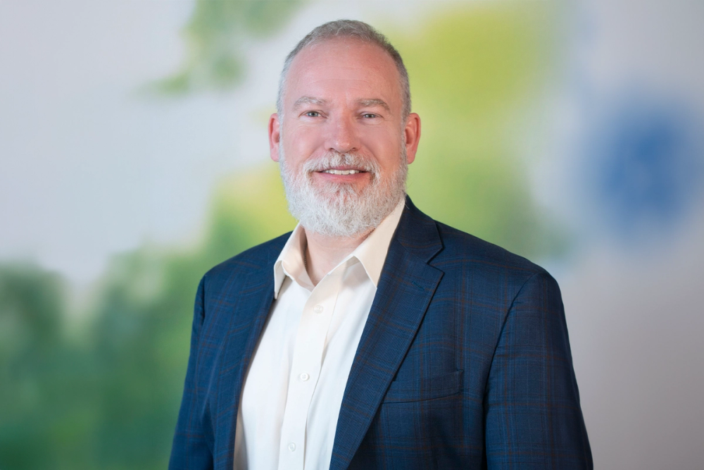 A man with a gray beard smiles in a suit