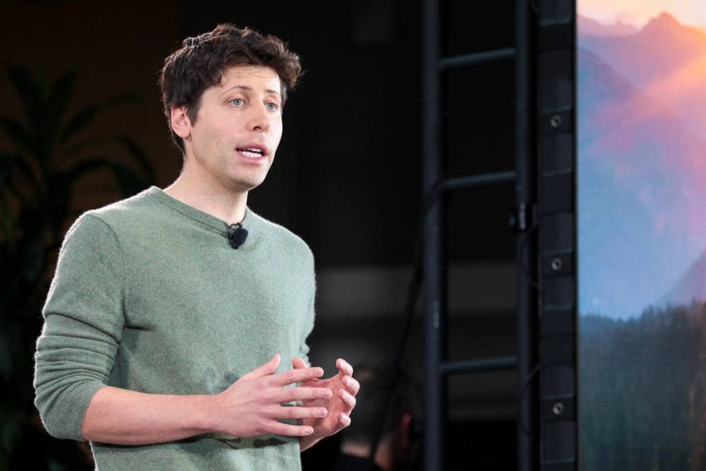 Open AI CEO Sam Altman, wearing a green sweatshirt, talks on a stage.