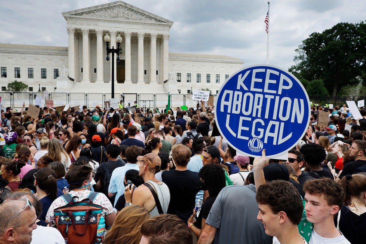 A large crowd of protesters stand in front of the Supreme Court, a young man holds a sign above his head in the shape of circle that reads, 'Keep Abortion legal'