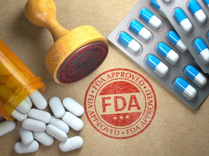 A rubber stamp saying FDA approved on brown paper surrounded by pills.