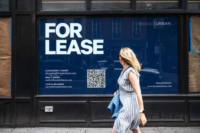 A woman walks by a "For Lease" sign on a building