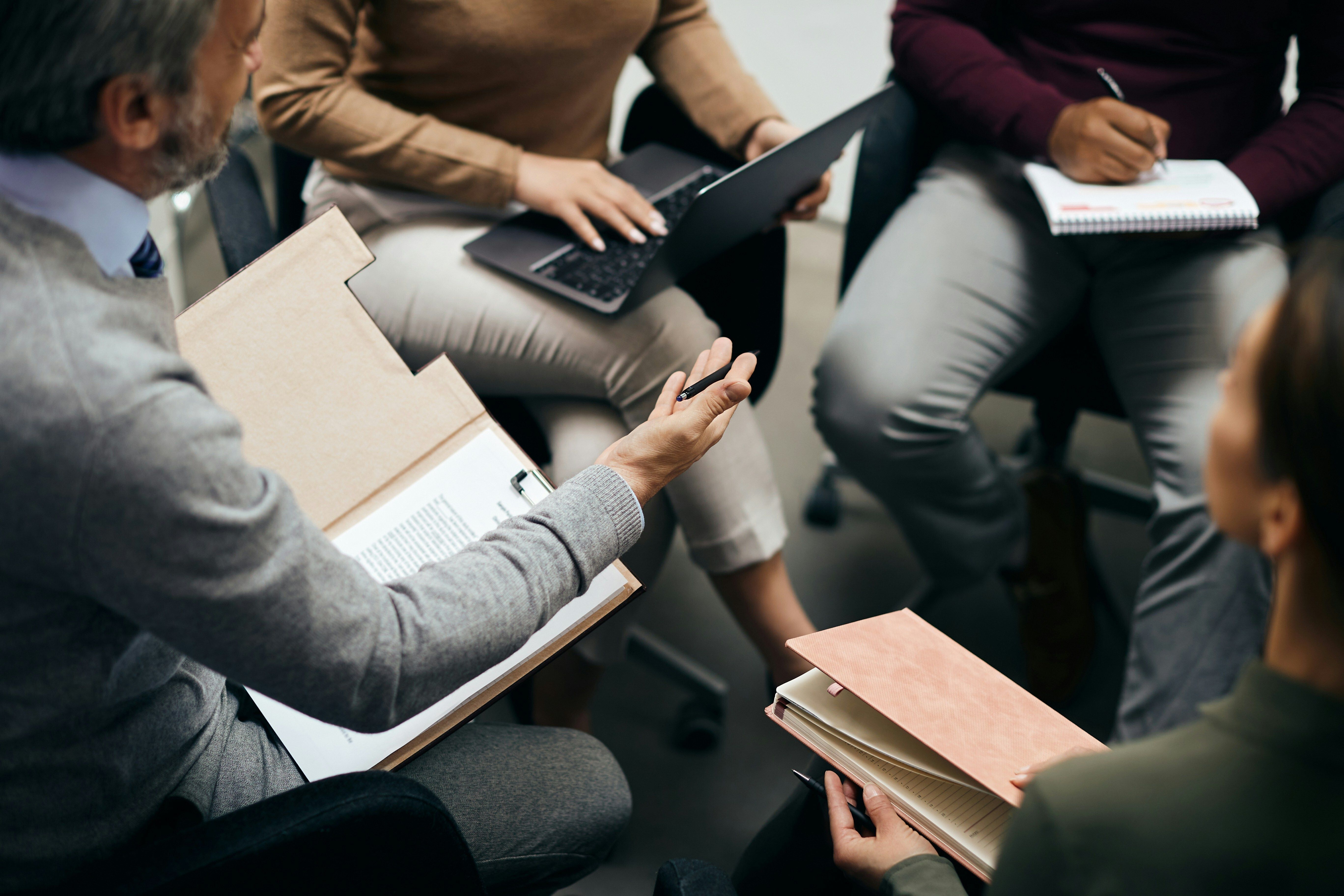 A diverse group of professionals seated in rows take notes on tablets and notebooks during a conference or workshop session.