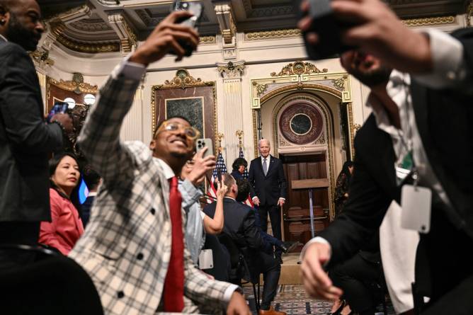 attendees at the White House creator conference pose in front of president Joe Biden speaking at a podium