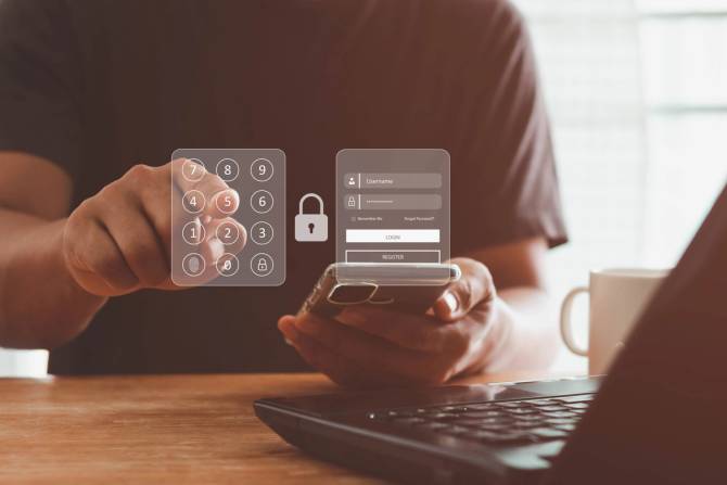 A person using a laptop enters a number code to unlock something using their cell phone.