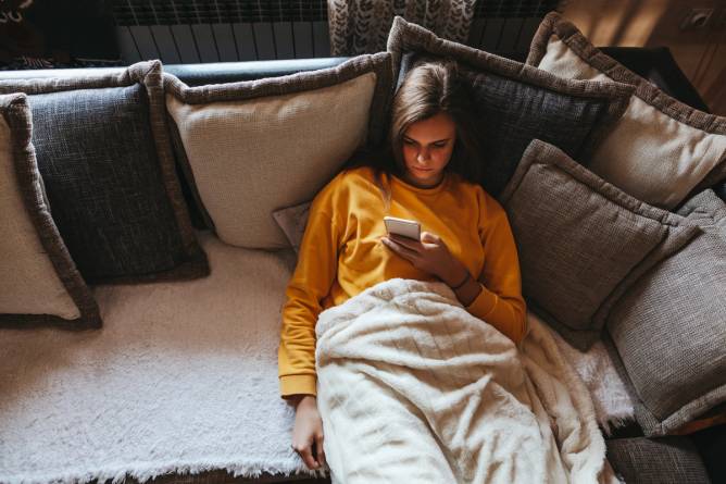 Photo of a woman lying on a couch scrolling through her phone.