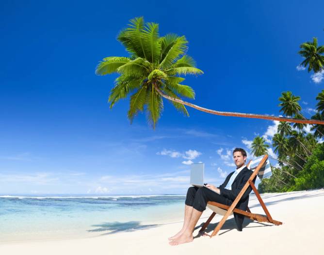 a man in a business suit with a laptop sits in a beach chair, surrounded by the ocean and palm trees.