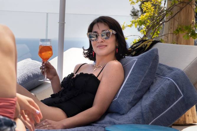 a scene from HBO's White Lotus featuring a character in a bathing suit drinking an Aperol Spritz