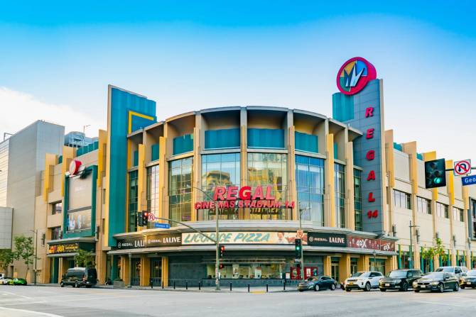 The facade of a Regal Cinemas theater in Los Angeles in front of a blue sky with a road and cars in front of it