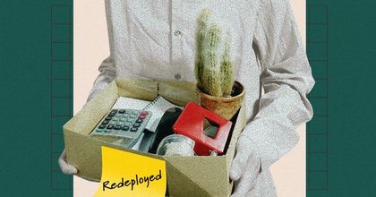 An employee getting laid off walking out with a box of desk items labeled "Redeployed"