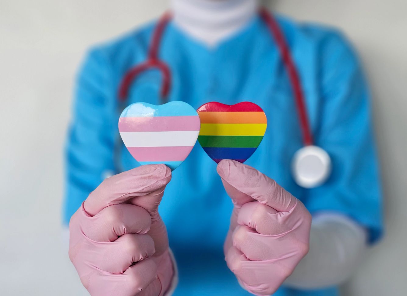 Healthcare worker holding transgender and rainbow pride symbols while advocating for inclusivity in medicine