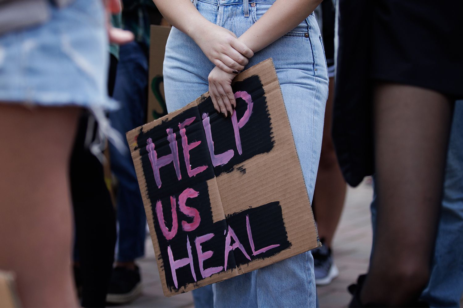 Close crop, young adult, handmade cardboard sign reading 'help us heal'