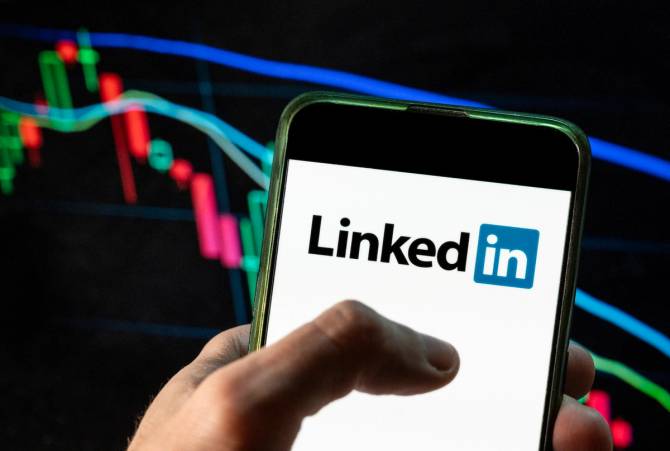 Close-up of a person's hand holding a phone that reads "LinkedIn" against a black background with multicolored lines.