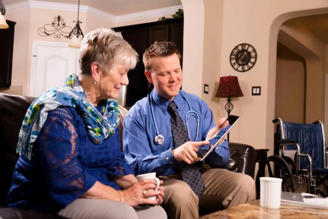 A young male doctor visits an older woman at her home.