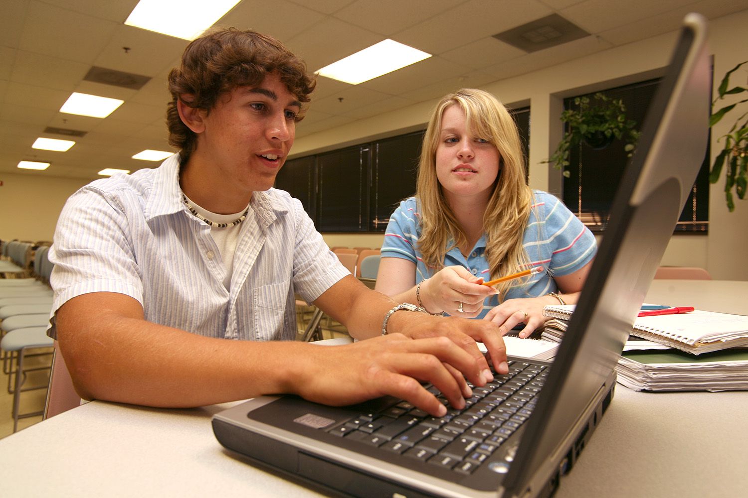 Two teenagers looking at a laptop ina classroom setting.