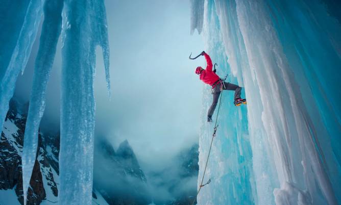 Two walls of ice; in the middle is a man vertically climbing up one sheet of ice