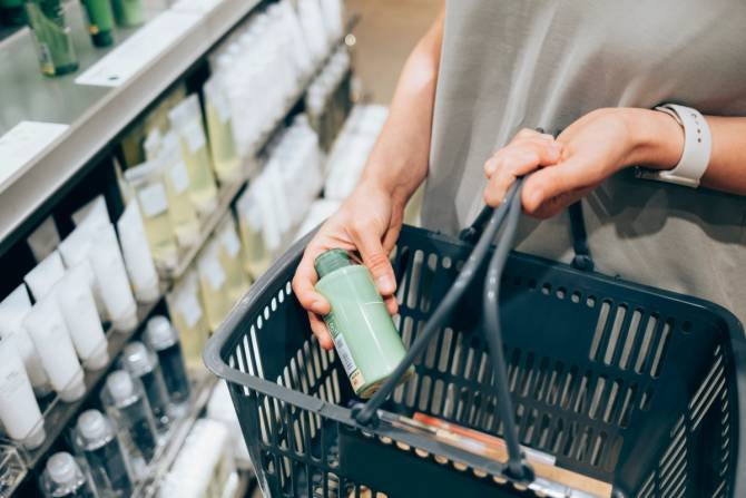 Closeup of a person’s hands placing a beauty product into a shopping basket.