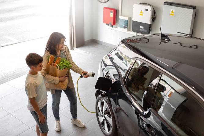 Woman holding grocery bag with child in garage preparing to charge EV.