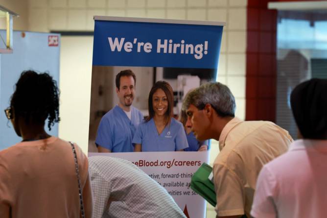 Job seekers stand in line at a booth at a job fair.