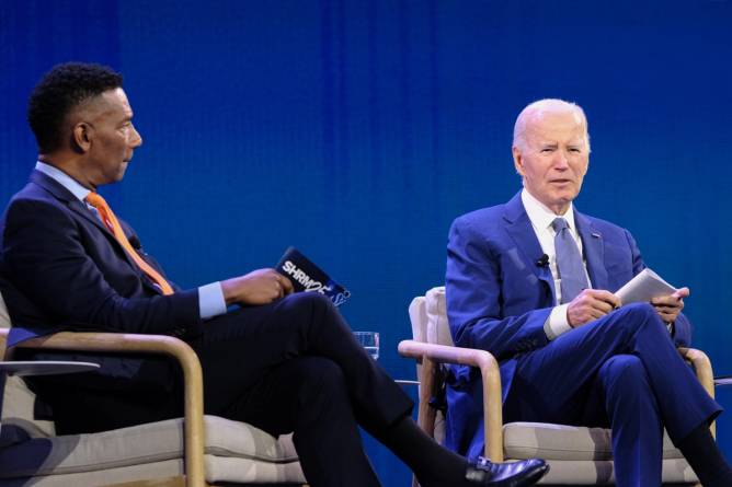 President Biden (right) sitting with Johnny C Taylor Jr (left) on a large stage and a table between them