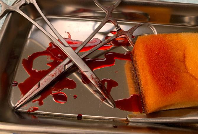 Medical scissors and sponge on a metal sheet covered in blood