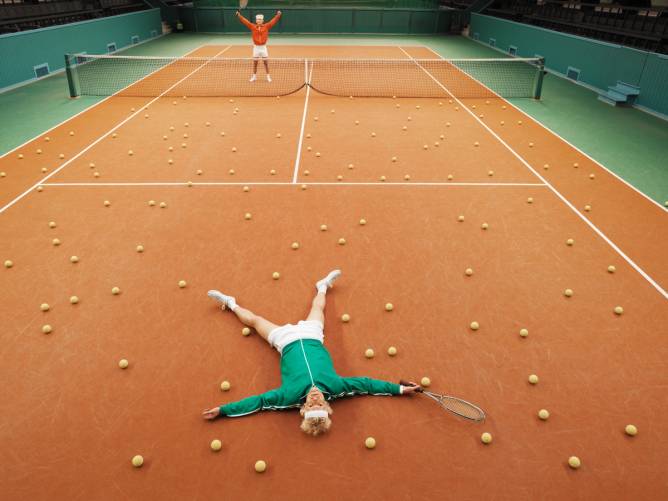A tennis player raises his arms in triumph as another player lies down in defeat.