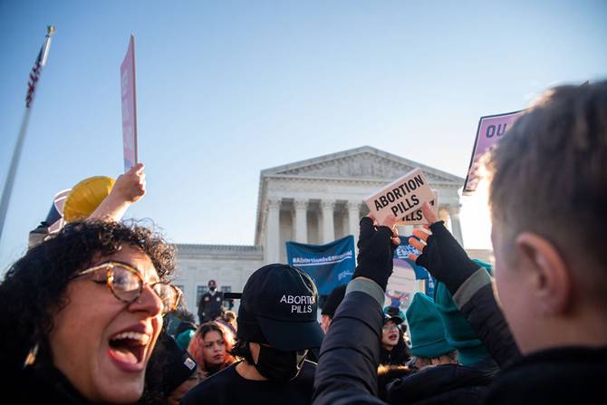 people holding signs in front of the Supreme Court that say "Abortion Pills"