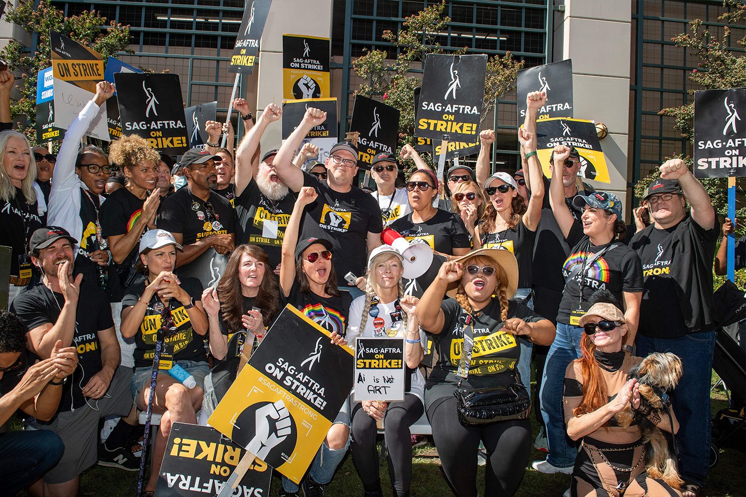 Members of the SAG-AFTRA at the picket line holding signs and raising their fists in the air.