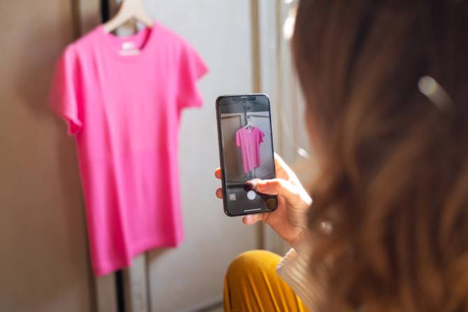 A woman photographs a pink shirt on her iPhone. 