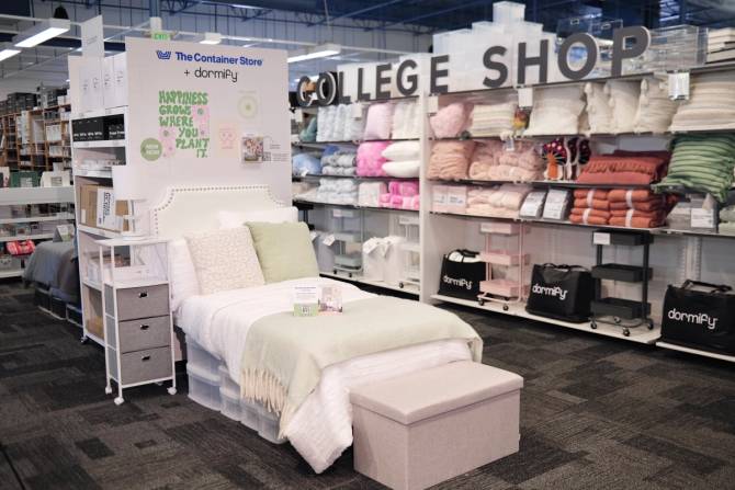 A Dormify store within a The Container Store location features a single bed made up in Dormify bedding and other products including a side table and lamp.