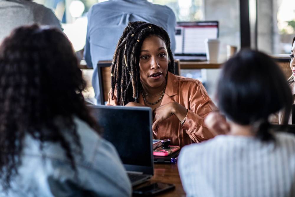 three Black women with different hair textures and styles working at a table