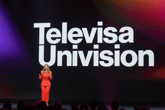TelevisaUnivision head of ad sales Donna Speciale stands onstage in a red suit with the TelevisaUnivision logo in white on a screen behind her