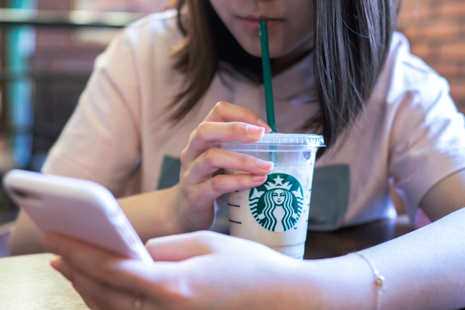 A girl drinks from a Starbucks cup while looking at her phone