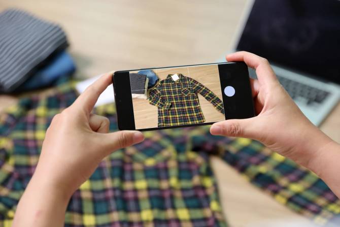 Someone takes a photograph of a shirt on a smartphone, an image typical for a product listing on a used-clothing website. 