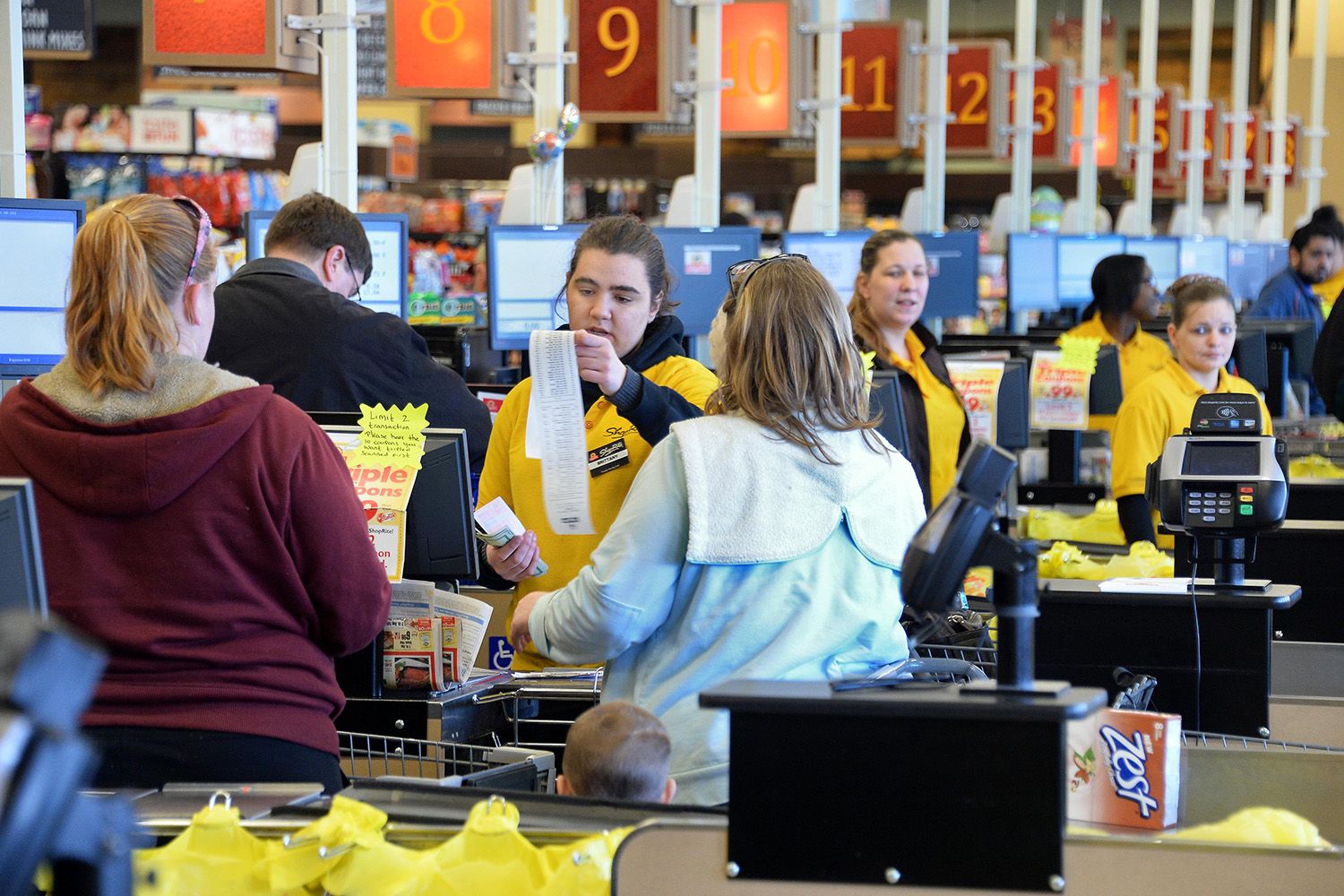 Busy supermarket checkout lanes, young employee cashiers.