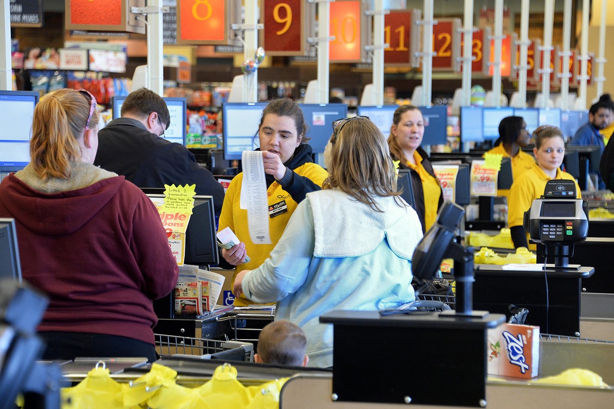 Busy supermarket checkout lanes, young employee cashiers.
