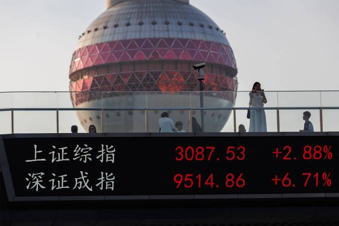 People walk on a pedestrian bridge which displays the numbers of Shanghai and Shenzhen stock indexes.