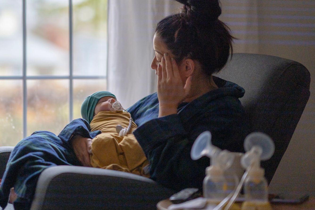 New mother is pictured holding her baby while rubbing her forehead.