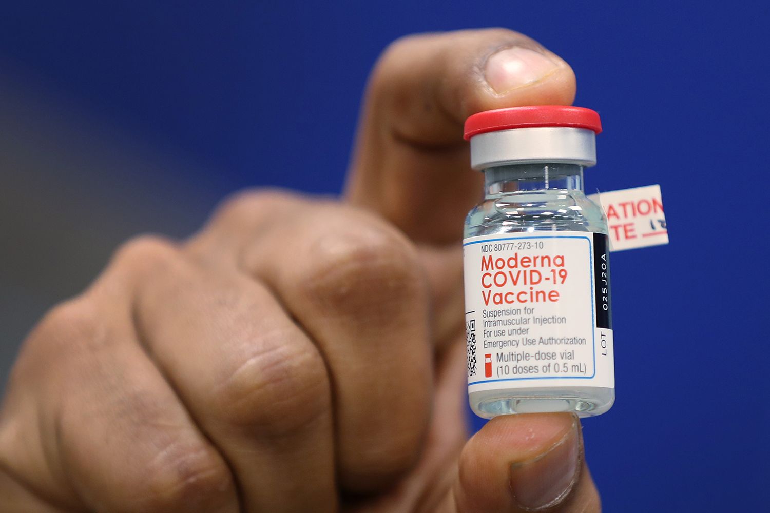 A hand holding a bottle of the Moderna COVID-19 vaccine.