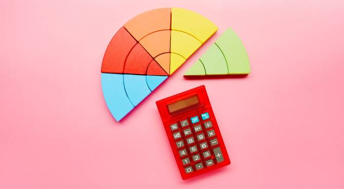 High angle view of a pie chart made of colorful building blocks and red calculator on pink background
