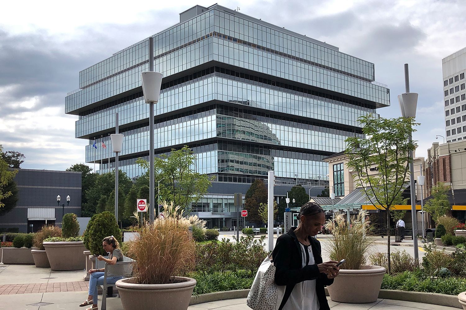 People sit in a park in front of the Purdue building, a tiered all-glass structure